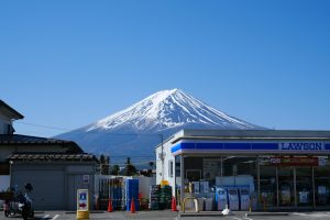Scenic view of Mount Fuji behind a convenience store under a clear blue sky.