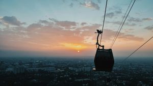 A cable car silhouetted against a vibrant sunset over a bustling cityscape, viewed from above.