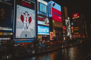 Illuminated signs and billboards reflecting on Dotonbori River in vibrant Osaka nightlife scene.